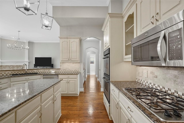 kitchen featuring ornamental molding, wood finished floors, stainless steel appliances, arched walkways, and a sink