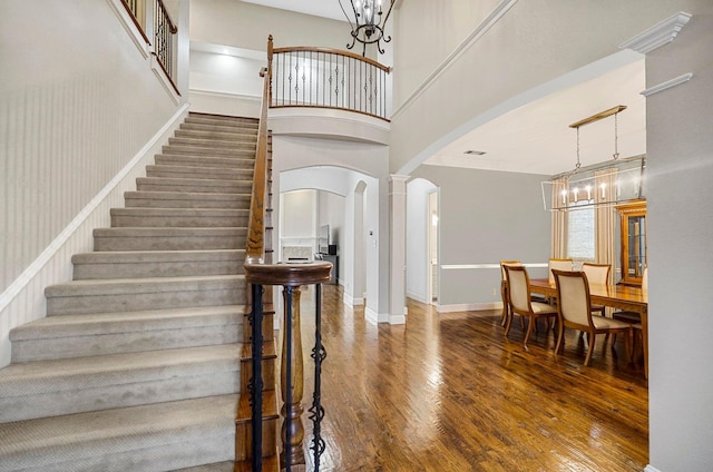 stairway with baseboards, wood finished floors, arched walkways, a high ceiling, and a notable chandelier