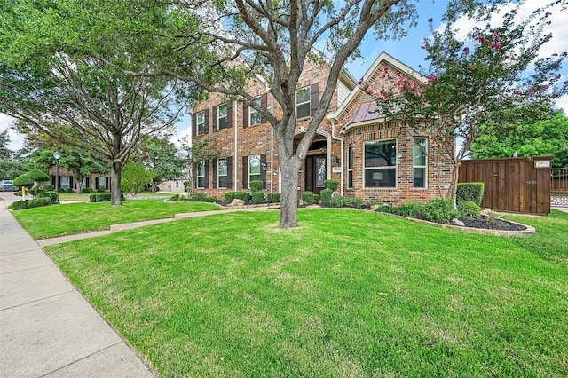 view of front facade featuring brick siding, a front yard, and fence