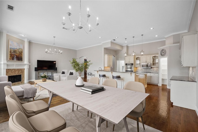 dining room featuring visible vents, crown molding, a fireplace, wood finished floors, and an inviting chandelier