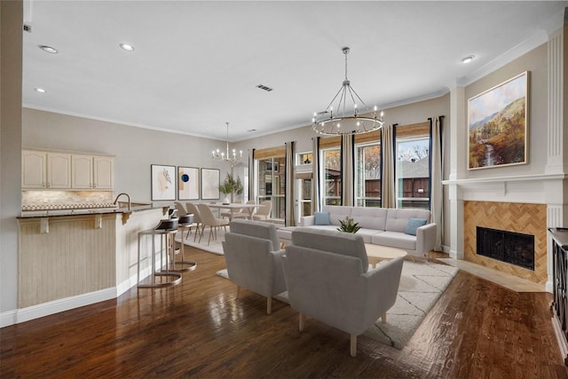 living area with visible vents, ornamental molding, wood finished floors, a tiled fireplace, and a notable chandelier