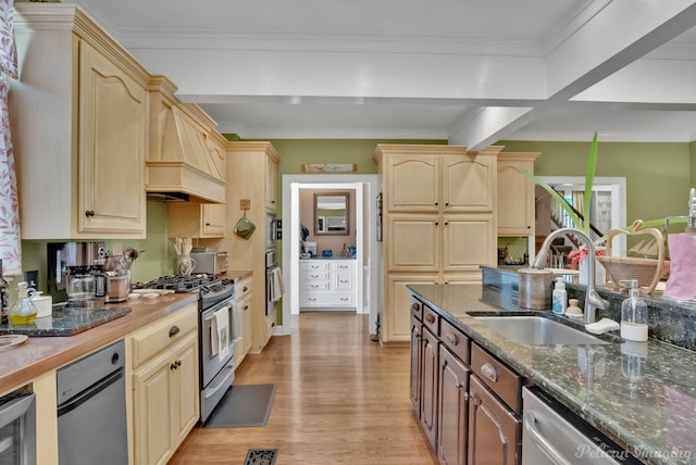kitchen with light brown cabinets, dark stone counters, stainless steel appliances, light wood finished floors, and a sink