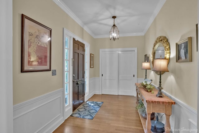 foyer entrance featuring ornamental molding, a wainscoted wall, a chandelier, and wood finished floors