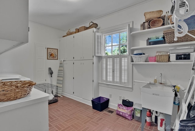 interior space featuring baseboards, a sink, crown molding, and brick patterned floor