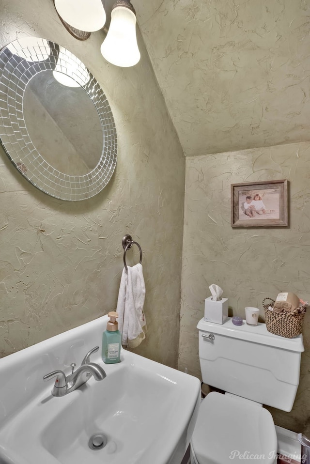 half bath with a sink, toilet, and lofted ceiling