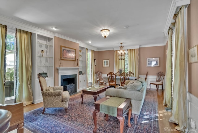 living area featuring a notable chandelier, ornamental molding, a fireplace, built in shelves, and wood finished floors