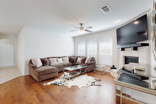 living room featuring arched walkways, visible vents, wood finished floors, ceiling fan, and a fireplace
