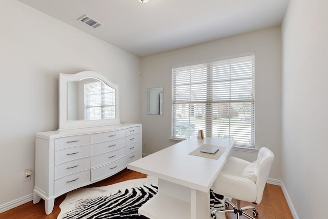 home office featuring baseboards, wood finished floors, visible vents, and a healthy amount of sunlight