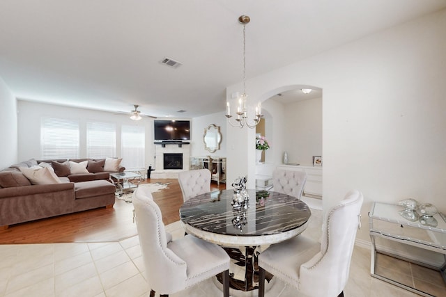 2037 Barx Dr, Little Elm, TX 75068 - dining room featuring a fireplace with raised hearth, arched walkways, ceiling fan, and light tile patterned floors