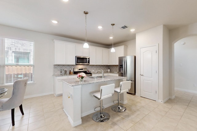 kitchen featuring tasteful backsplash, a sink, a kitchen island with sink, arched walkways, and stainless steel appliances