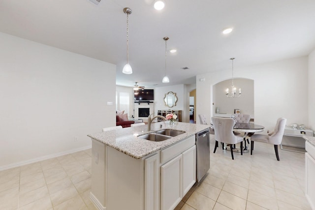 kitchen featuring arched walkways, a sink, dishwasher, a fireplace, and an island with sink