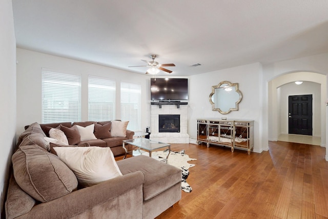 living room with arched walkways, visible vents, wood finished floors, ceiling fan, and a fireplace