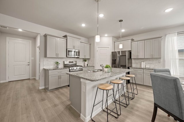 5312 Waterview Ct, Haltom City, TX 76137 - kitchen featuring appliances with stainless steel finishes, a breakfast bar, an island with sink, tasteful backsplash, and light stone counters