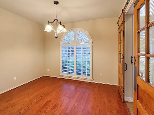 empty room with a barn door, baseboards, wood finished floors, and a chandelier