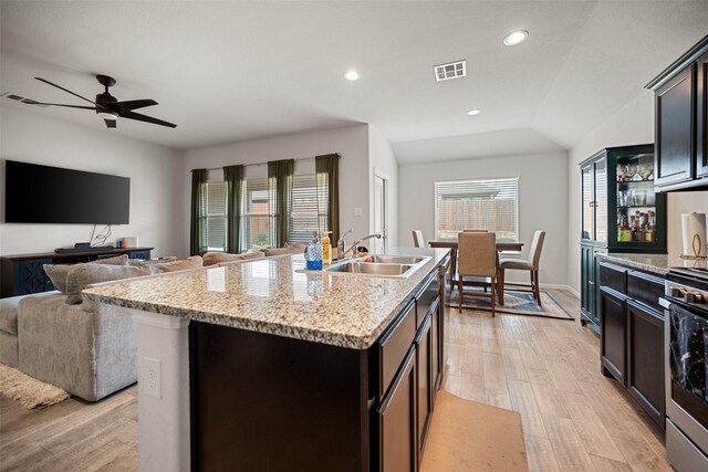 kitchen featuring visible vents, light wood finished floors, a sink, open floor plan, and vaulted ceiling