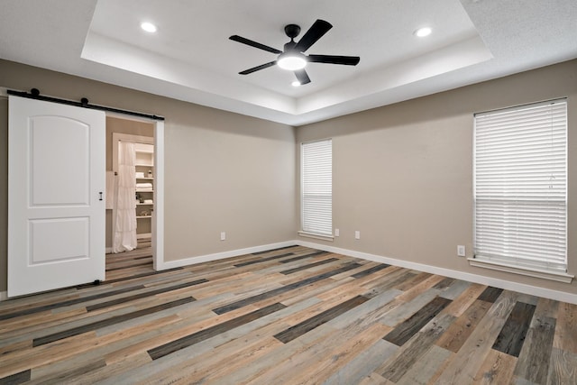 unfurnished room featuring baseboards, wood finished floors, a ceiling fan, a raised ceiling, and a barn door