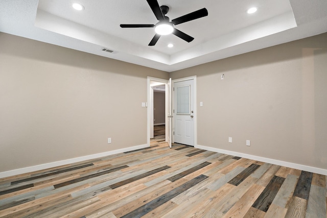 unfurnished room with a ceiling fan, a raised ceiling, light wood-style flooring, baseboards, and visible vents