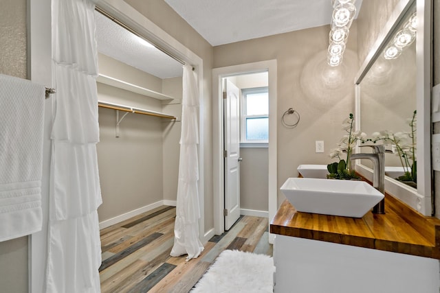 bathroom featuring a textured ceiling, baseboards, double vanity, wood finished floors, and a sink
