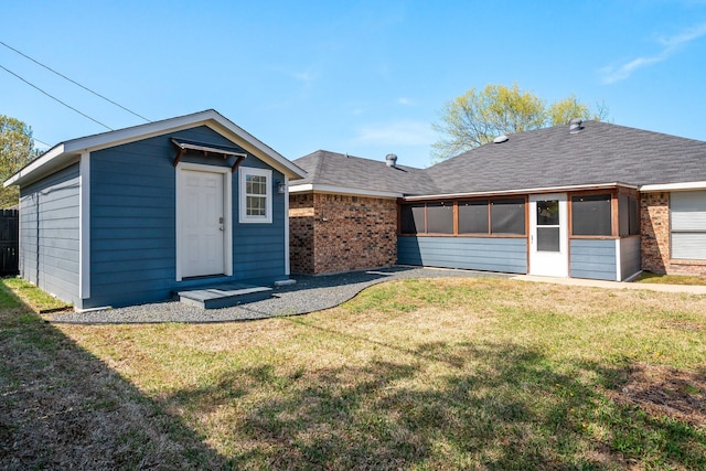 rear view of property with an outbuilding, brick siding, a shingled roof, a sunroom, and a yard