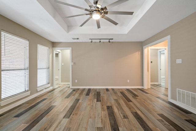 empty room with wood finished floors, a tray ceiling, and visible vents