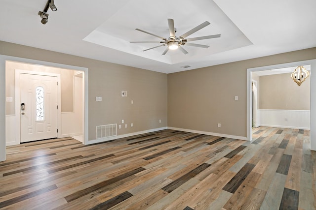 interior space featuring ceiling fan with notable chandelier, light wood-style flooring, a tray ceiling, and visible vents