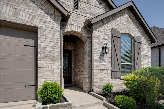 view of exterior entry featuring a garage and brick siding