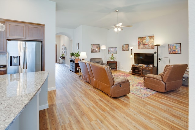 living area with light wood-type flooring, arched walkways, and a ceiling fan