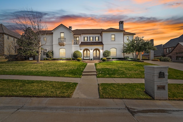 view of front facade featuring stucco siding, a balcony, a front lawn, and a chimney