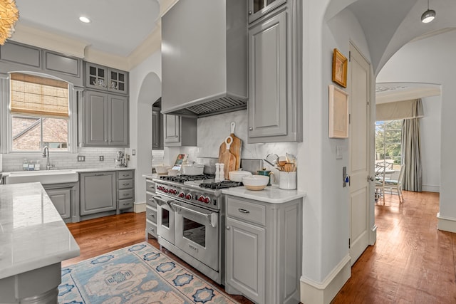 kitchen featuring double oven range, custom range hood, gray cabinets, a sink, and arched walkways