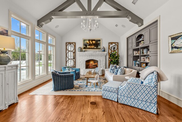 living room with a notable chandelier, a warm lit fireplace, lofted ceiling with beams, wood finished floors, and visible vents