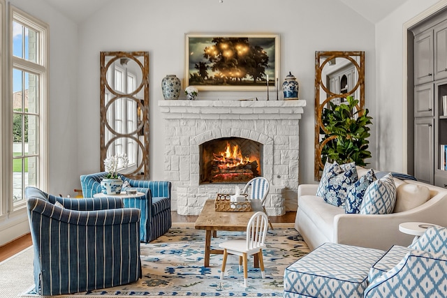 living room featuring a warm lit fireplace, wood finished floors, and vaulted ceiling