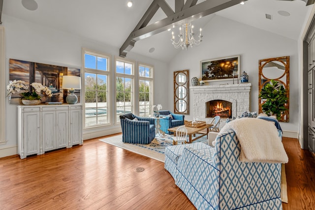 living area with a notable chandelier, high vaulted ceiling, beamed ceiling, a stone fireplace, and wood finished floors