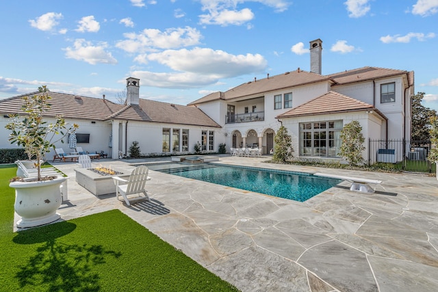 back of house featuring a patio area, an outdoor fire pit, a chimney, fence, and a tiled roof