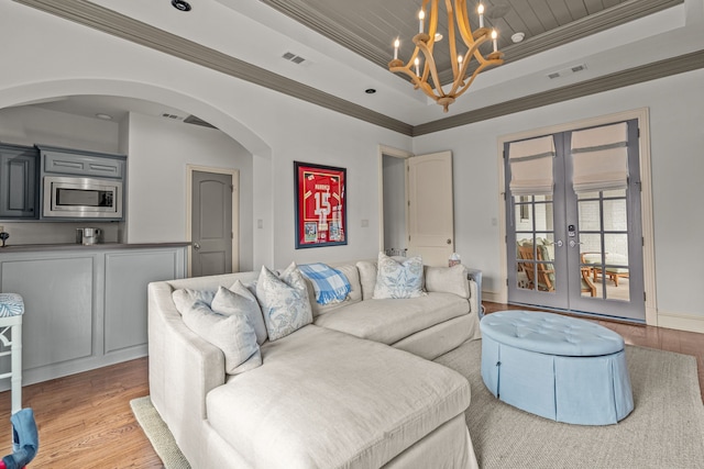 living room featuring a tray ceiling, french doors, a chandelier, visible vents, and light wood-style flooring