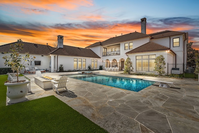 pool at dusk with fence, a pool with connected hot tub, a fire pit, a diving board, and a patio area