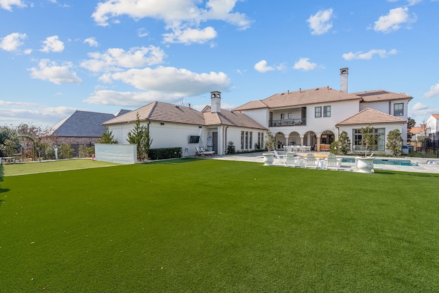 back of property featuring a balcony, fence, a patio, a fenced in pool, and a yard
