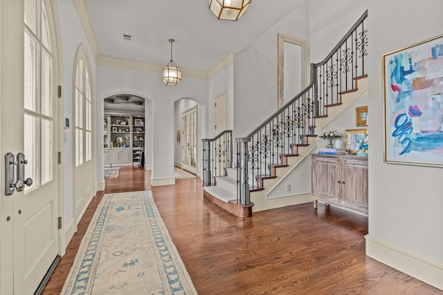entryway with crown molding, stairway, dark wood-type flooring, baseboards, and arched walkways