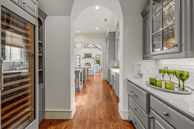 bar with backsplash, wood finished floors, baseboards, arched walkways, and recessed lighting