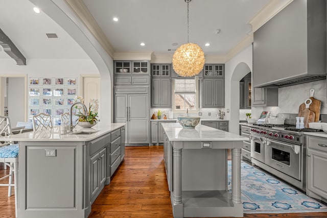 kitchen with gray cabinetry, a kitchen island with sink, a sink, and range with two ovens