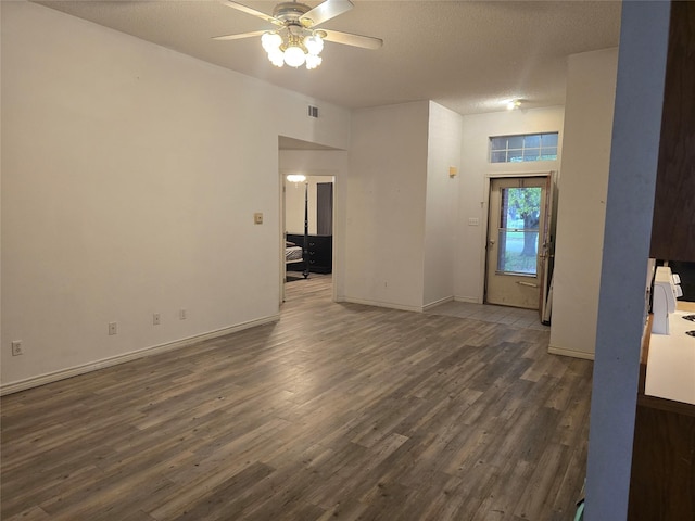 empty room featuring a textured ceiling, ceiling fan, baseboards, dark wood-type flooring, and visible vents