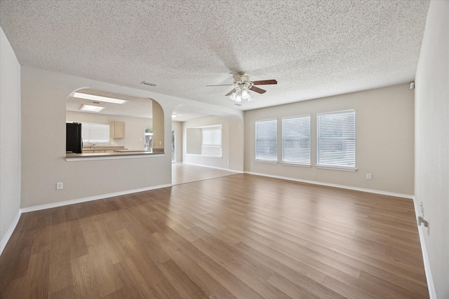 unfurnished living room with ceiling fan, wood finished floors, arched walkways, baseboards, and a textured ceiling