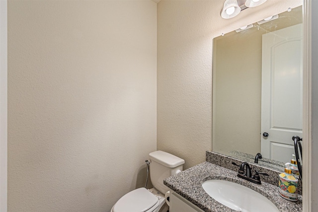 half bath featuring toilet, vanity, and a textured wall