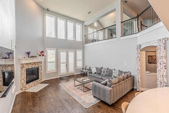 living area featuring a fireplace with flush hearth, a high ceiling, baseboards, and dark wood-type flooring
