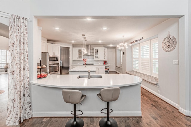 kitchen with stainless steel appliances, backsplash, a sink, wall chimney range hood, and a peninsula