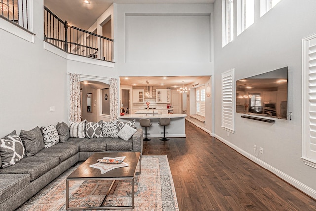 living area with baseboards, a wealth of natural light, a chandelier, and dark wood finished floors