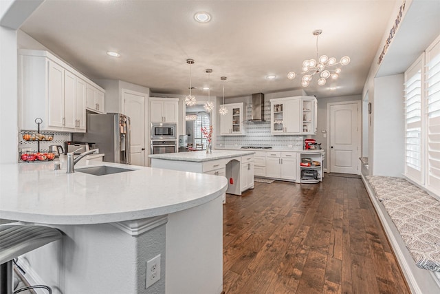 kitchen with a sink, a chandelier, wall chimney exhaust hood, a peninsula, and stainless steel appliances