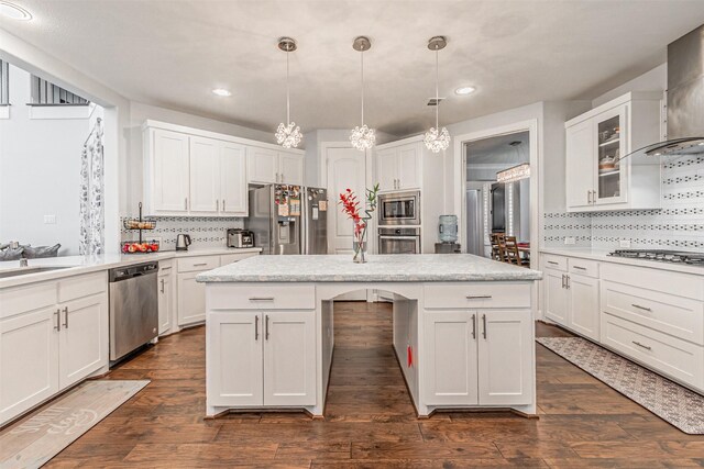 kitchen with light countertops, white cabinetry, wall chimney exhaust hood, appliances with stainless steel finishes, and a center island