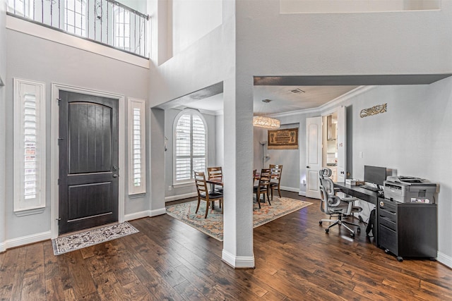 foyer entrance featuring crown molding, hardwood / wood-style flooring, a chandelier, baseboards, and a towering ceiling