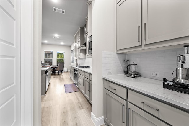 kitchen featuring light wood-style flooring, backsplash, gray cabinetry, visible vents, and stainless steel appliances
