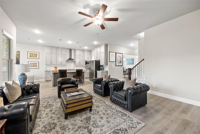 living area featuring baseboards, a ceiling fan, light wood-style floors, recessed lighting, and stairs